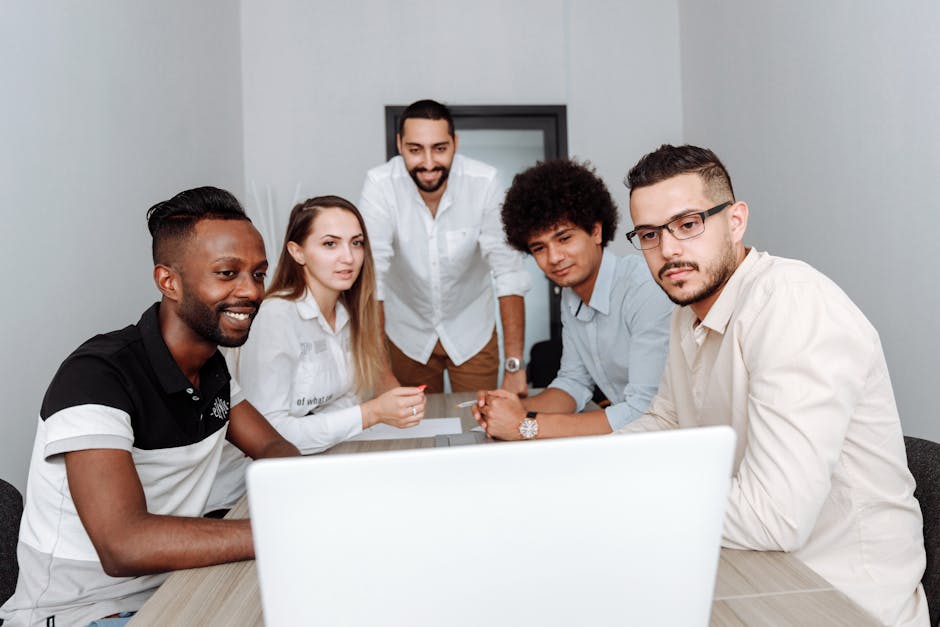 A diverse group of professionals engaging in a collaborative meeting around a laptop in an office